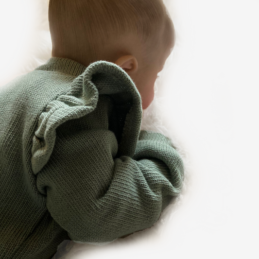 Detail van een baby in een olijfgroen gebreid boxpakje met ruches op de schouders. Zachte en comfortabele handgemaakte babykleding.