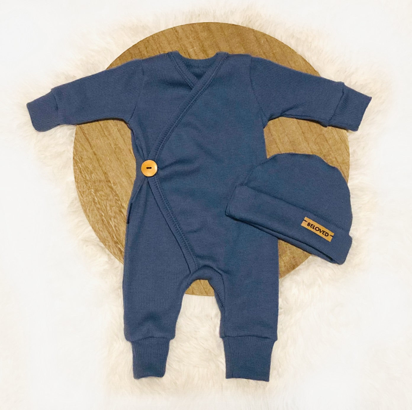 Flatlay foto van Boxpakje Arin - overslag romper met mutsje blauwe zachte ribstof en bruine accentjes. Duurzame handgemaakte babykleding van webshop Cuteez.