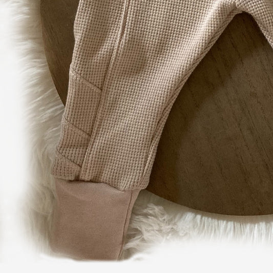 Een close-up van het Retro jogger broekje van kinderkleding webshop Cuteez, met zijn zachte, beige wafelstof en oogstrelende details. Ontdek duurzame kinderkleding in elk steekje. Handgemaakte baby- en kinderkleding.