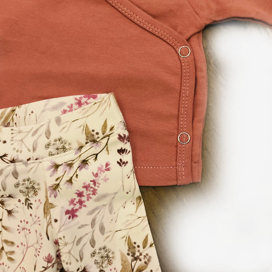 Close-up van het zachte biologische French terry truitje in mauve/roze met fijne afwerking en het broekje met bloemenprint en comfortabele boordjes.