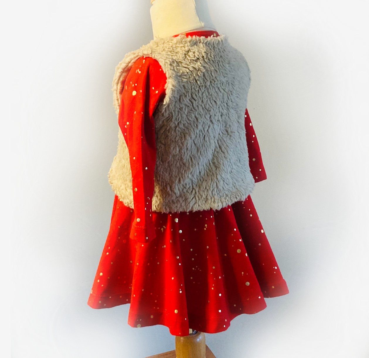 Achterzijde van rood kerstjurkje met gouden stippen en beige fleece gilet. Handgemaakte kinderkleding in maten 62-140.