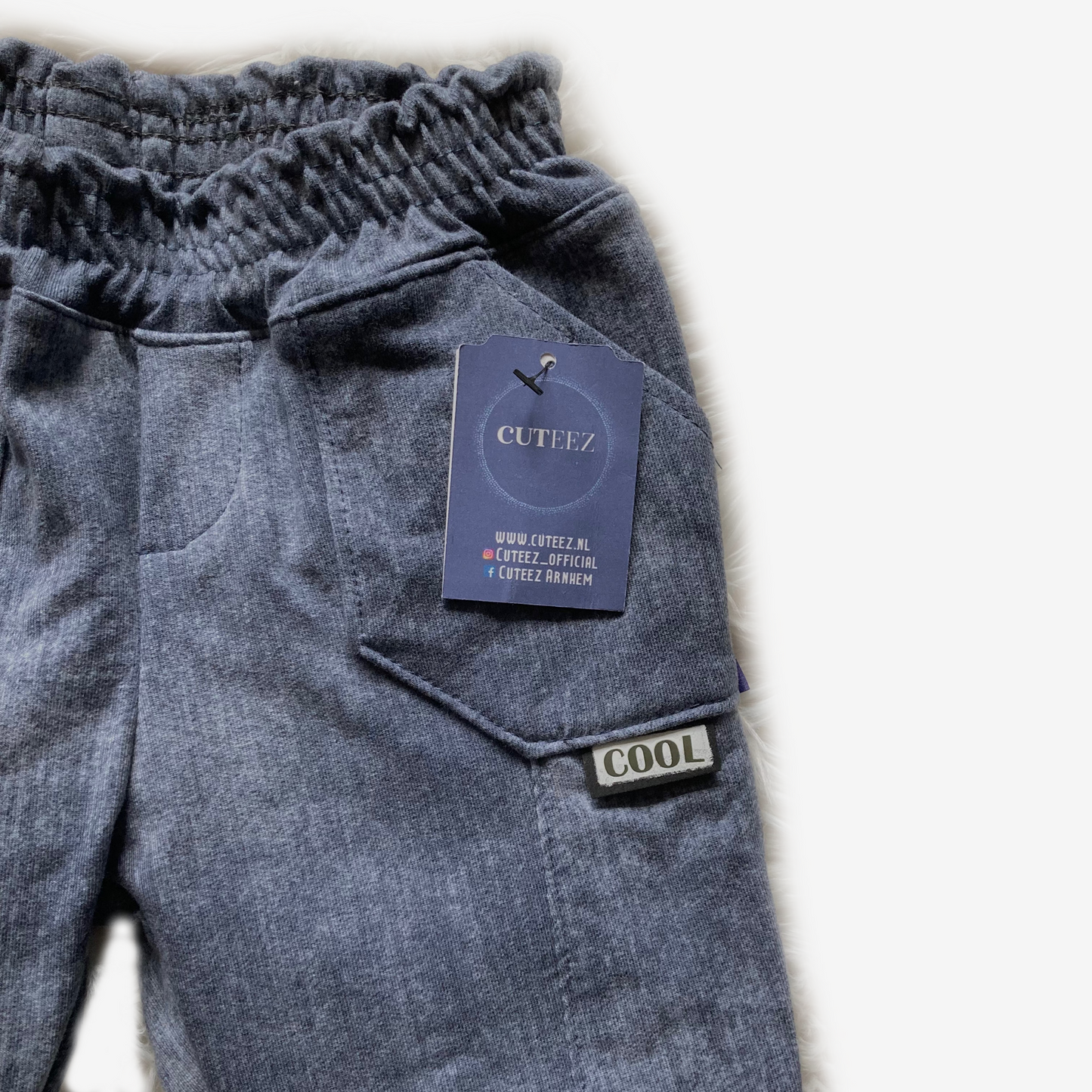 Detail van gewassen blauwe stretch jeansstof met stoere zakken en Cuteez-label – zachte, comfortabele kinderkleding